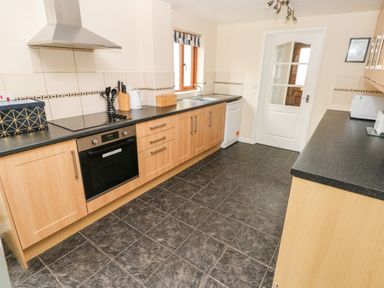A kitchen with wooden cabinets black countertops an electric stove oven a dishwasher and a sink at Brynawel in Llangynin near Llanboidy