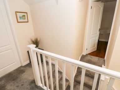 A staircase landing with gray carpet a white railing a small table with decorative grass and a painting on the wall at Brynawel in Llangynin near Llanboidy