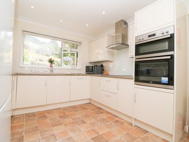 A kitchen with white cabinets a double oven a microwave a knife block a window and a tiled floor at Rathillet in Feock near Truro