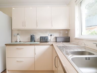 A kitchen with a double sink a drying rack a kettle a toaster and cream cabinets at Rathillet in Feock near Truro