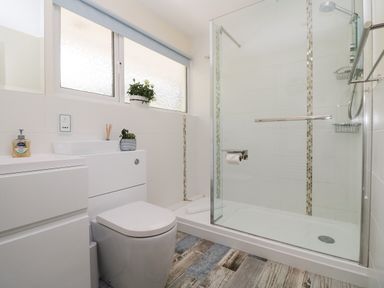 A bathroom with a toilet, a shower with glass doors, a sink, and plants on the windowsill at Rathillet in Feock near Truro
