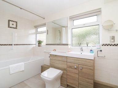 A bathroom with a bathtub a toilet a double sink wooden cabinets and two frosted windows at Rathillet in Feock near Truro