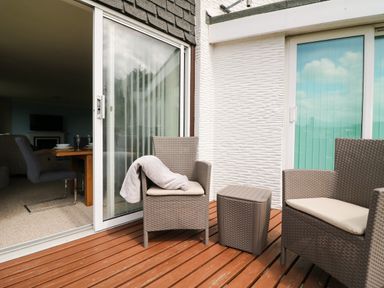 An outdoor patio with two wicker chairs and a small table on wooden decking at Rathillet in Feock near Truro