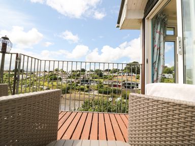 A balcony with two wicker chairs and a metal railing overlooking houses and greenery at Rathillet in Feock near Truro