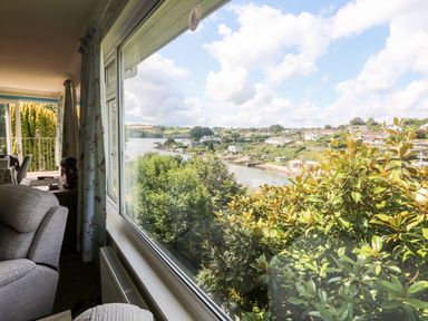 A living room with armchairs and curtains overlooking a river and houses at Rathillet in Feock near Truro