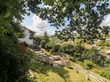 A backyard with stone patio, wooden picnic table, and fenced garden overlooking a river at Rathillet in Feock near Truro