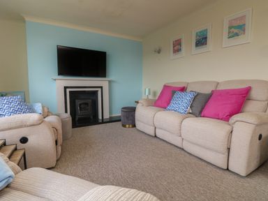 A living room with beige sofas with colorful cushions a fireplace with a mounted TV and framed pictures on the wall at Rathillet in Feock near Truro