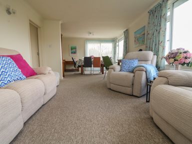 A living room with beige sofas and colorful cushions a dining table with multiple chairs and floral curtains at Rathillet in Feock near Truro