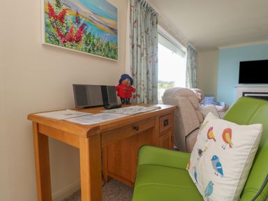 A wooden desk with papers a speaker and a stuffed bear next to a green chair with a bird cushion in a living room at Rathillet in Feock near Truro