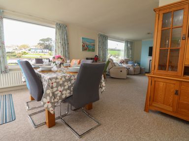 A dining area with a table set for six and chairs next to a living room with armchairs and a wooden cabinet at Rathillet Feock near Truro