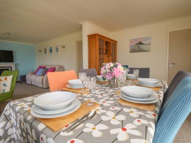 A dining table set with plates glasses and cutlery in a living room with armchairs a sofa a wooden cabinet and wall art at Rathillet in Feock near Truro