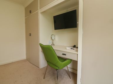 A study area with a green chair a built-in desk and a wall-mounted television at Rathillet in Feock near Truro