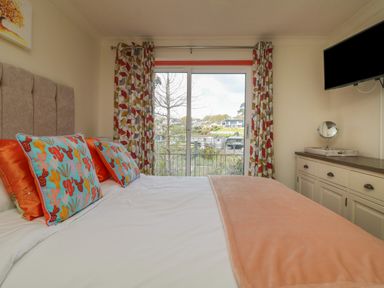A bedroom with a bed facing a sliding glass door with patterned curtains and a wall-mounted TV at Rathillet Feock near Truro