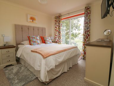A bedroom with a double bed two bedside tables a dresser a wall mounted television and large window with patterned curtains at Rathillet in Feock near Truro