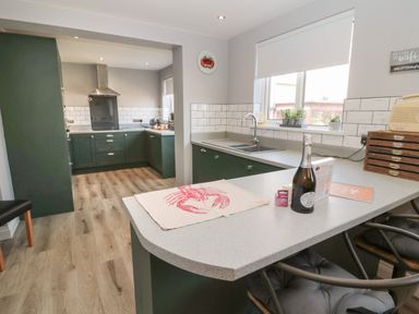 A kitchen with green cabinets, a countertop with a bottle and chairs, and a window at Fisherman's Row in Amble