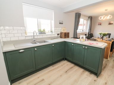 A kitchen with green cabinets and a double sink next to a dining area with a wooden table and chairs at Fisherman's Row in Amble