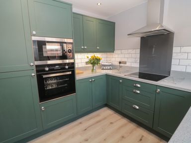 A kitchen with green cabinets and appliances including an oven microwave toaster and stove at Fisherman's Row in Amble