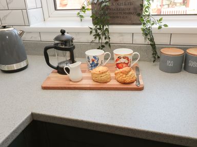 A kitchen countertop with a kettle french press mugs scones a knife and jars labeled tea and sugar at Fisherman's Row in Amble