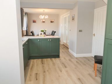 A kitchen with green cabinets and a dining area with black chairs and a modern light at Fisherman's Row in Amble
