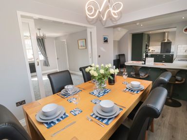 A dining table set for six with white flowers in a vase in a kitchen and dining area at Fisherman's Row in Amble