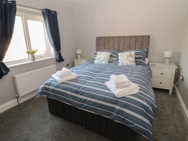 A bedroom with a double bed with striped bedding and towels on top with nightstands and lamps at Fisherman's Row in Amble