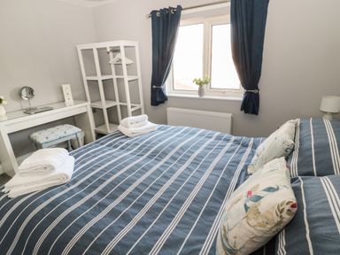 A bedroom with a bed covered in striped bedding and pillows and a vanity with a stool at Fisherman's Row in Amble