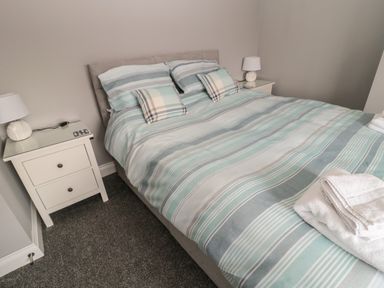 A bedroom with a double bed with striped bedding and two bedside tables with lamps at Fisherman's Row in Amble