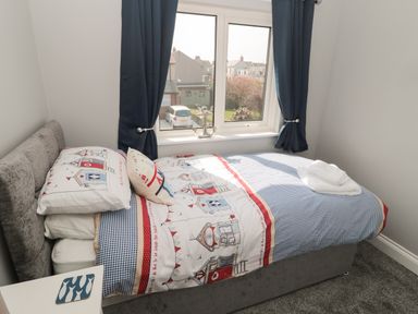 A small bedroom with a single bed beside a window with blue curtains at Fisherman's Row in Amble