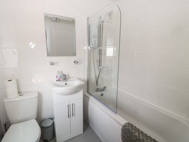 A bathroom with a toilet, sink with cabinet, mirror, bathtub with shower, and a shower curtain at Fisherman's Row in Amble