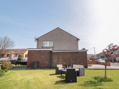 A backyard with outdoor seating and a small tree next to a gray and brick house at Fisherman's Row in Amble