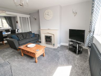 A living room with a grey sofa wooden coffee table fireplace TV and curtains at Fisherman's Row in Amble