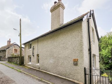 A stone cottage with chimneys next to a narrow road at Myrtle Villa in Knighton