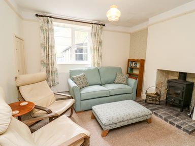A living room with two cream chairs a blue sofa an ottoman a wood stove and a bookshelf at Myrtle Villa in Knighton