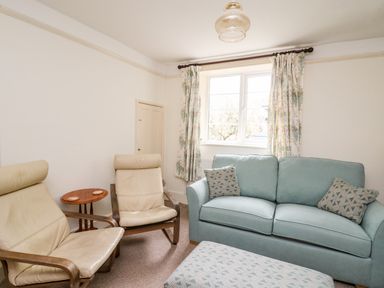 A sitting room with two beige armchairs a blue sofa with patterned cushions and an ottoman near a window at Myrtle Villa in Knighton