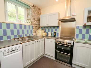 A kitchen with white cabinets a dishwasher a stainless steel oven sink and blue and green tiled backsplash at Myrtle Villa in Knighton