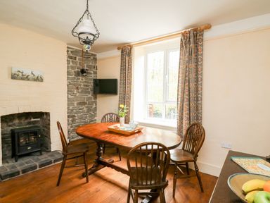 A dining area with wooden table and chairs a window with patterned curtains and a small fireplace at Myrtle Villa in Knighton