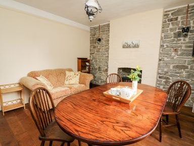 A dining room with a wooden table and chairs a sofa and stone walls at Myrtle Villa in Knighton