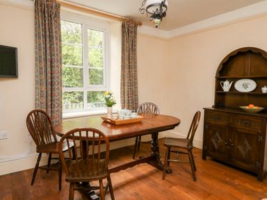 A dining room with a wooden table and chairs near a window with patterned curtains at Myrtle Villa in Knighton