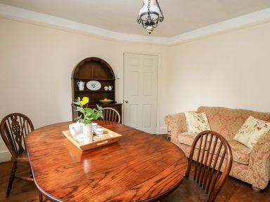 A dining room with wooden table and chairs a sofa and corner cabinet at Myrtle Villa in Knighton