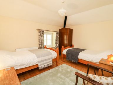 A bedroom with two single beds a wooden wardrobe and a chair at Myrtle Villa in Knighton