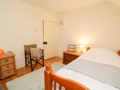 A bedroom with a wooden bed, two wooden nightstands, a chair with cushions, and a door at Myrtle Villa in Knighton