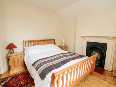 A bedroom with a wooden bed and two wooden bedside tables with lamps and a fireplace at Myrtle Villa in Knighton