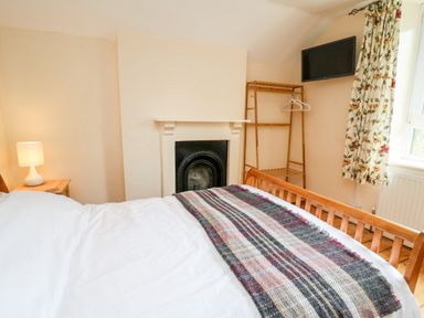 A bedroom with a bed a wooden clothes rack a wall-mounted television and floral curtains at Myrtle Villa in Knighton