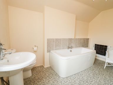 A bathroom with a bathtub a sink a toilet a towel rail and a white chair at Myrtle Villa in Knighton