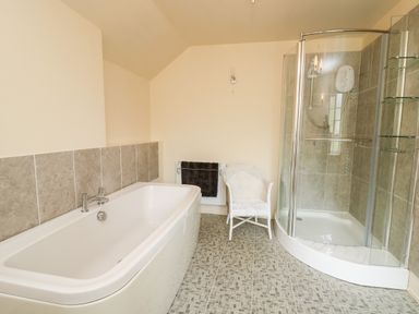 A bathroom with a bathtub, a glass shower enclosure, a white chair, and a towel hanging on a radiator Myrtle Villa Knighton