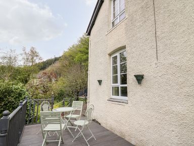 An outdoor patio with a metal table and chairs next to a cream stucco house with windows at Myrtle Villa in Knighton