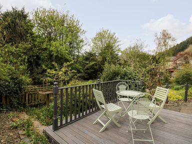 A garden patio with metal table and chairs surrounded by trees and plants at Myrtle Villa in Knighton