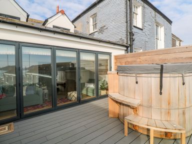 An outdoor patio with wooden deck flooring a round wooden hot tub with steps a glass wall showing a living area inside 16 Arwenack Street in Falmouth