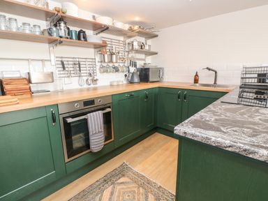 A kitchen with green cabinets wooden countertops open shelves with kitchenware and utensils at 16 Arwenack Street in Falmouth