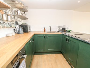 A kitchen with green cabinets wooden countertops a stainless steel sink a microwave kettle and hanging mugs at 16 Arwenack Street in Falmouth